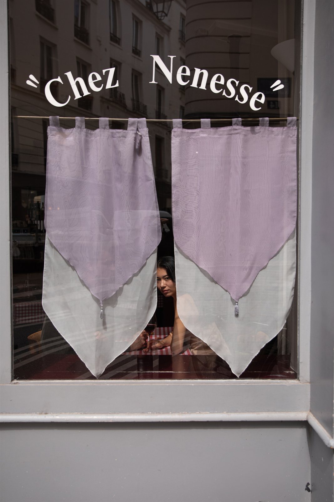 View of the Chez Nenesse restaurant frontage in Paris, with a wine tasting scene glimpsed through the window.